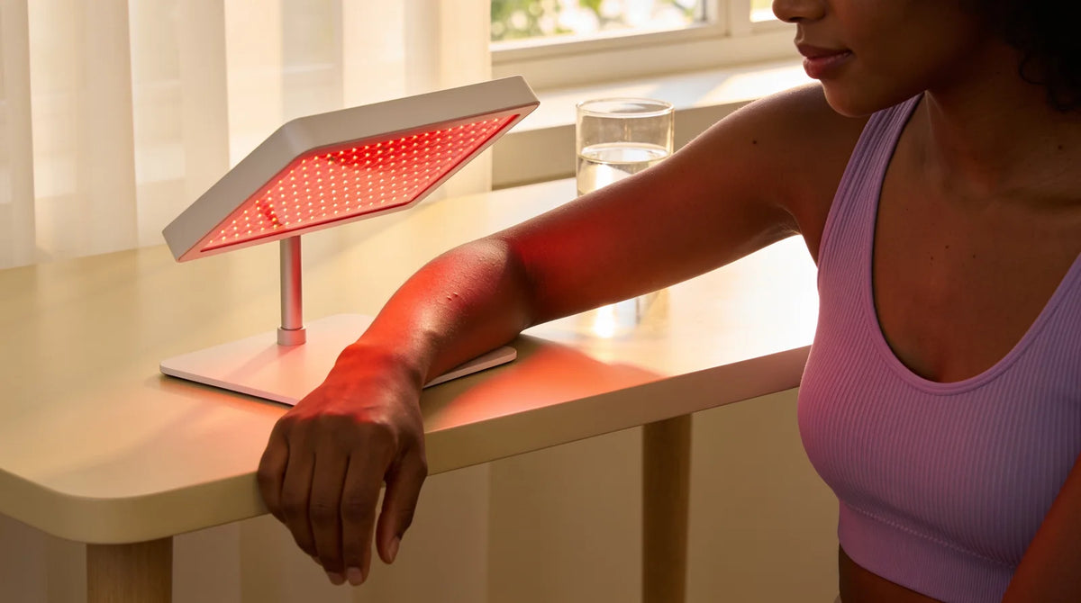 Woman resting her forearm under a small red LED light therapy panel on a table