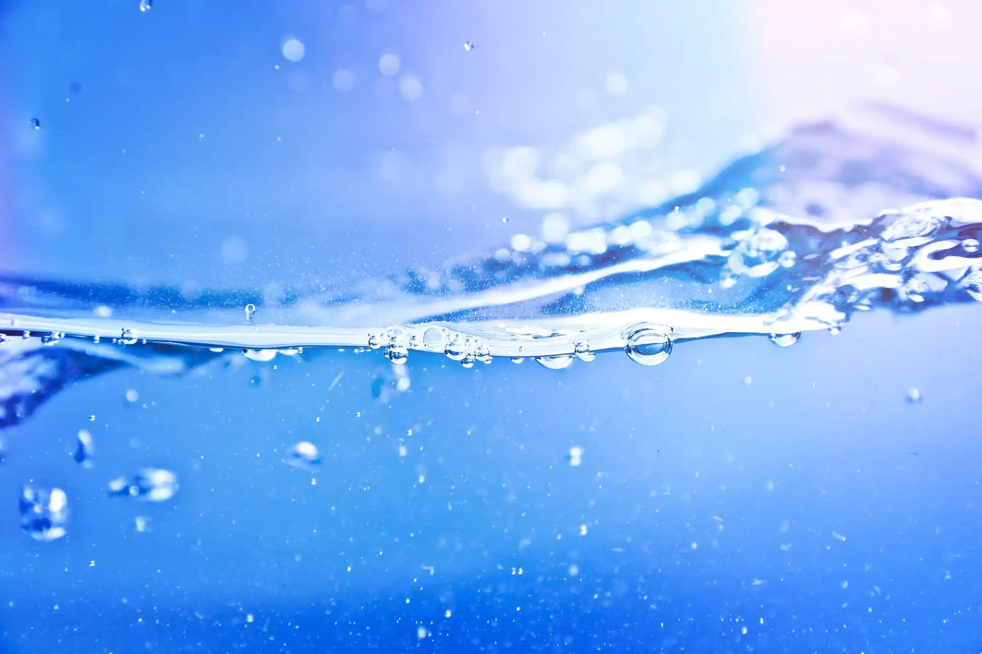 Water surface with cascading droplets and bubbles in bright blue, suspended against a misty sky.