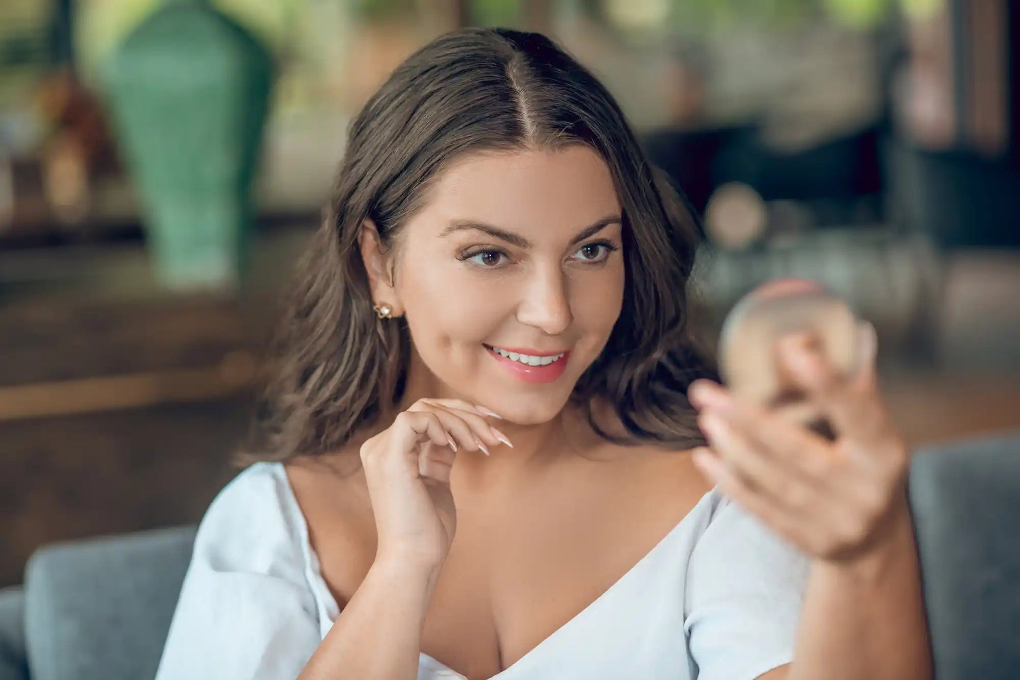Smiling woman with brown hair and a white top, looking at the camera while resting her hand near her chin.