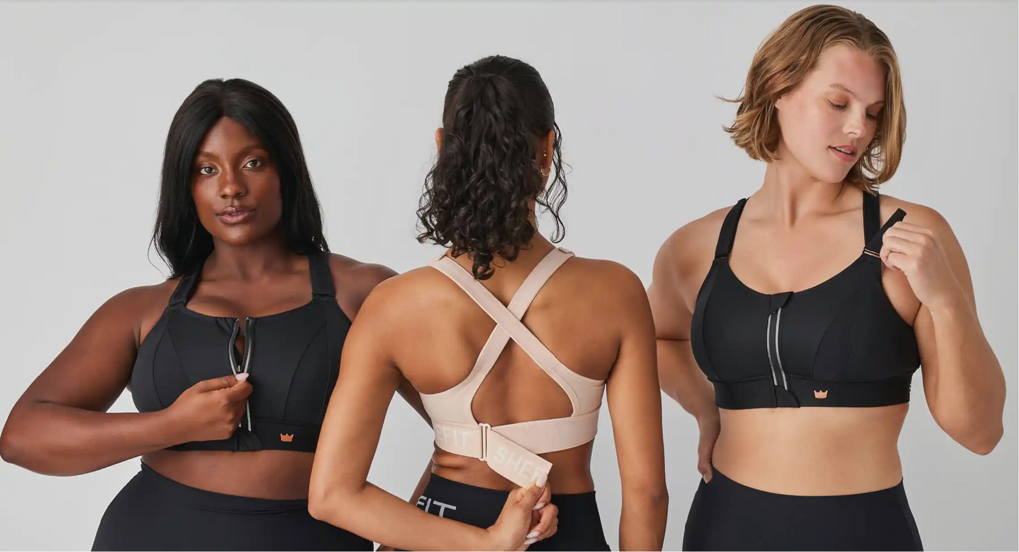Three women in sports bras adjust straps and hold clothing labels in a bright studio against a plain white backdrop.
