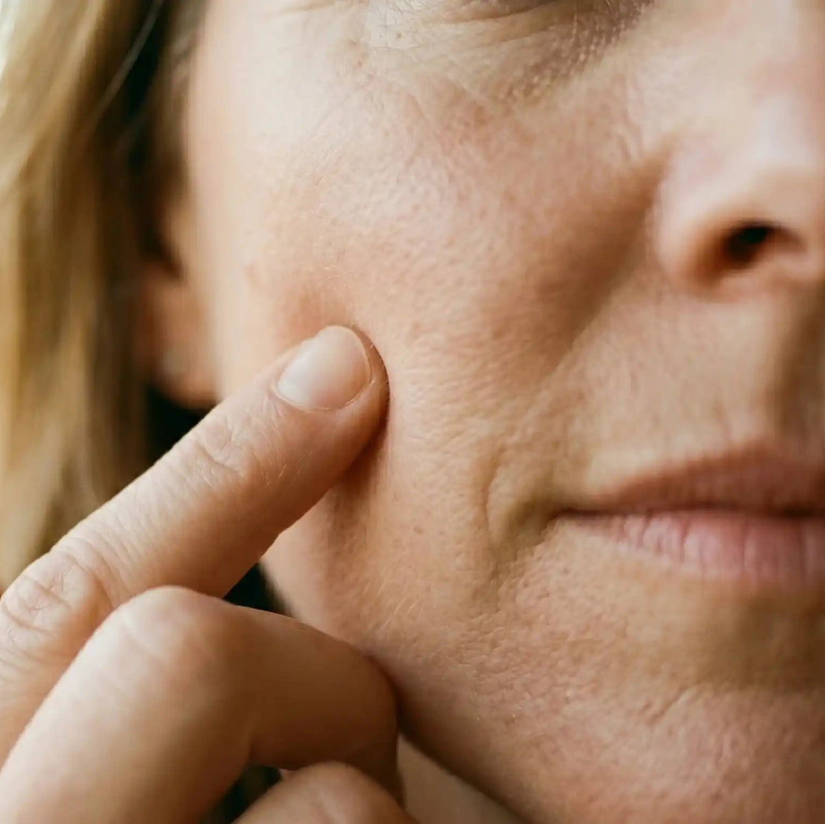 Close-up of an elderly man’s face as a finger gently touches his cheek, with soft blurred background.
