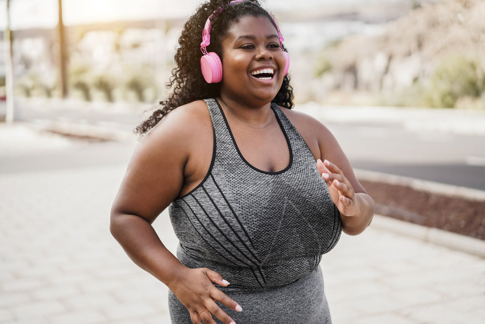 Smiling woman jogging outdoors with pink over ear headphones and a gray athletic tank top